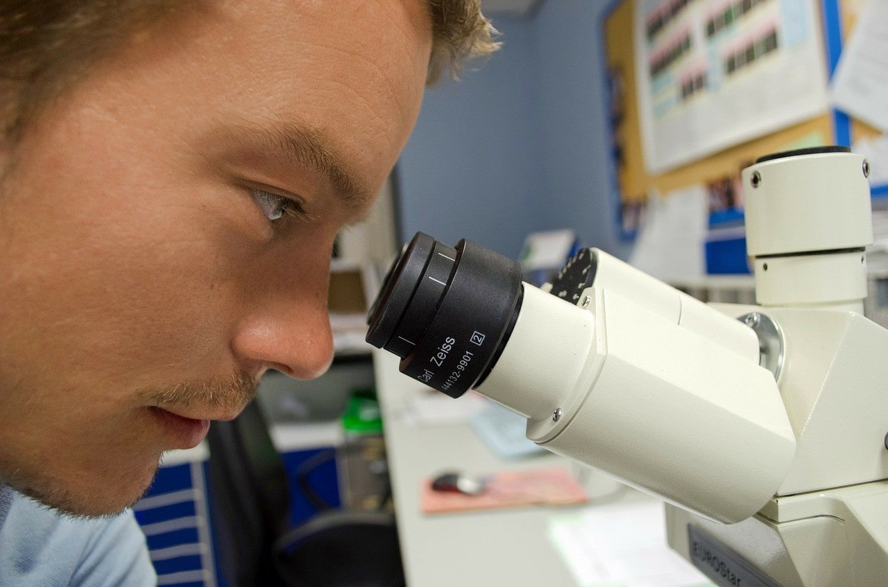 A scientist looking trough a microscope. He is wearing a white coat