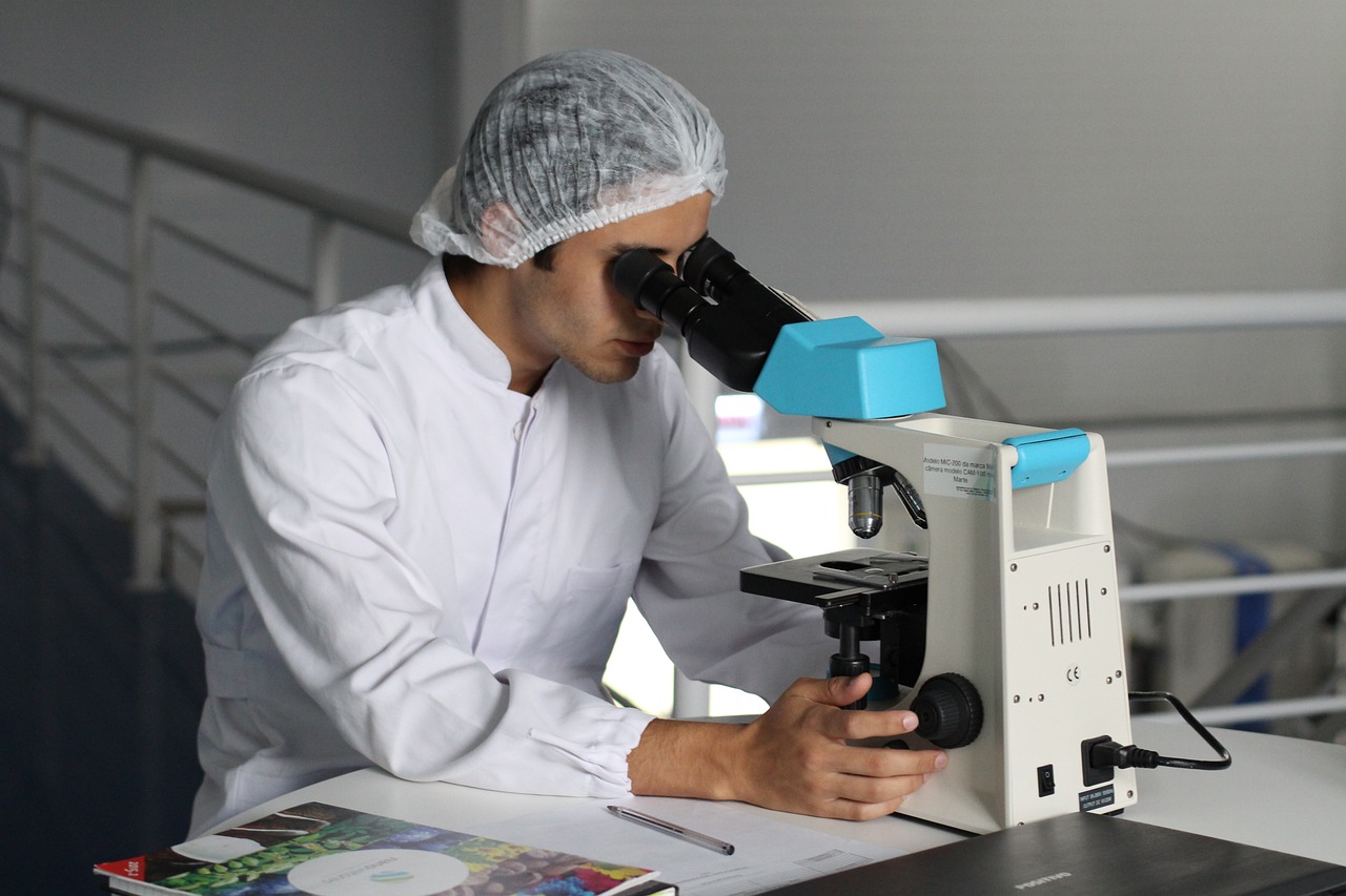 A scientist, wearing a white lab coat and a protective hairnet